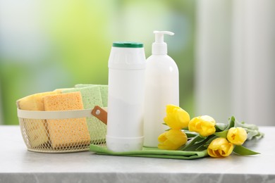 Photo of Spring cleaning. Detergents, supplies and yellow tulips on grey marble table indoors