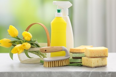 Photo of Spring cleaning. Detergents, supplies and yellow tulips on grey marble table indoors