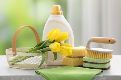 Photo of Spring cleaning. Detergents, supplies and yellow tulips on grey marble table indoors