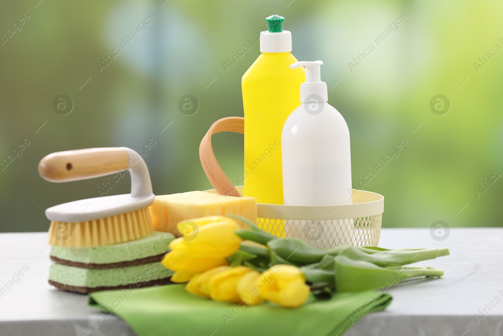 Photo of Spring cleaning. Detergents, supplies and yellow tulips on grey table indoors