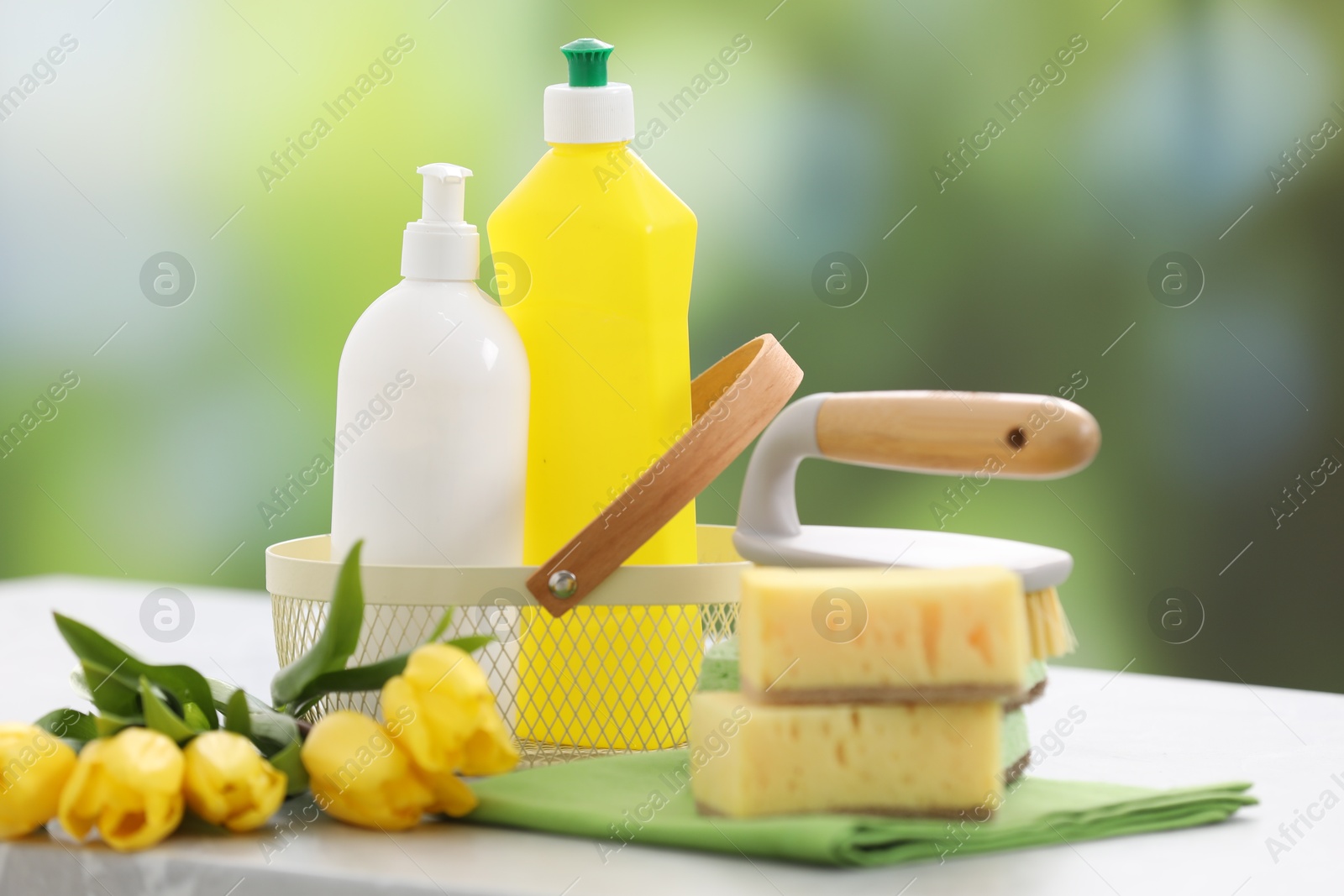 Photo of Spring cleaning. Detergents, supplies and yellow tulips on table indoors