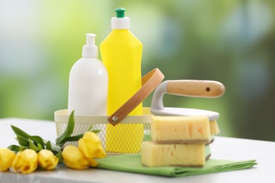 Photo of Spring cleaning. Detergents, supplies and yellow tulips on table indoors