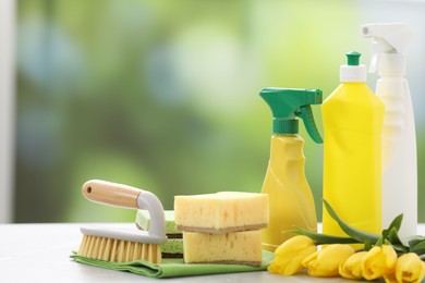 Photo of Spring cleaning. Detergents, supplies and yellow tulips on table indoors, closeup