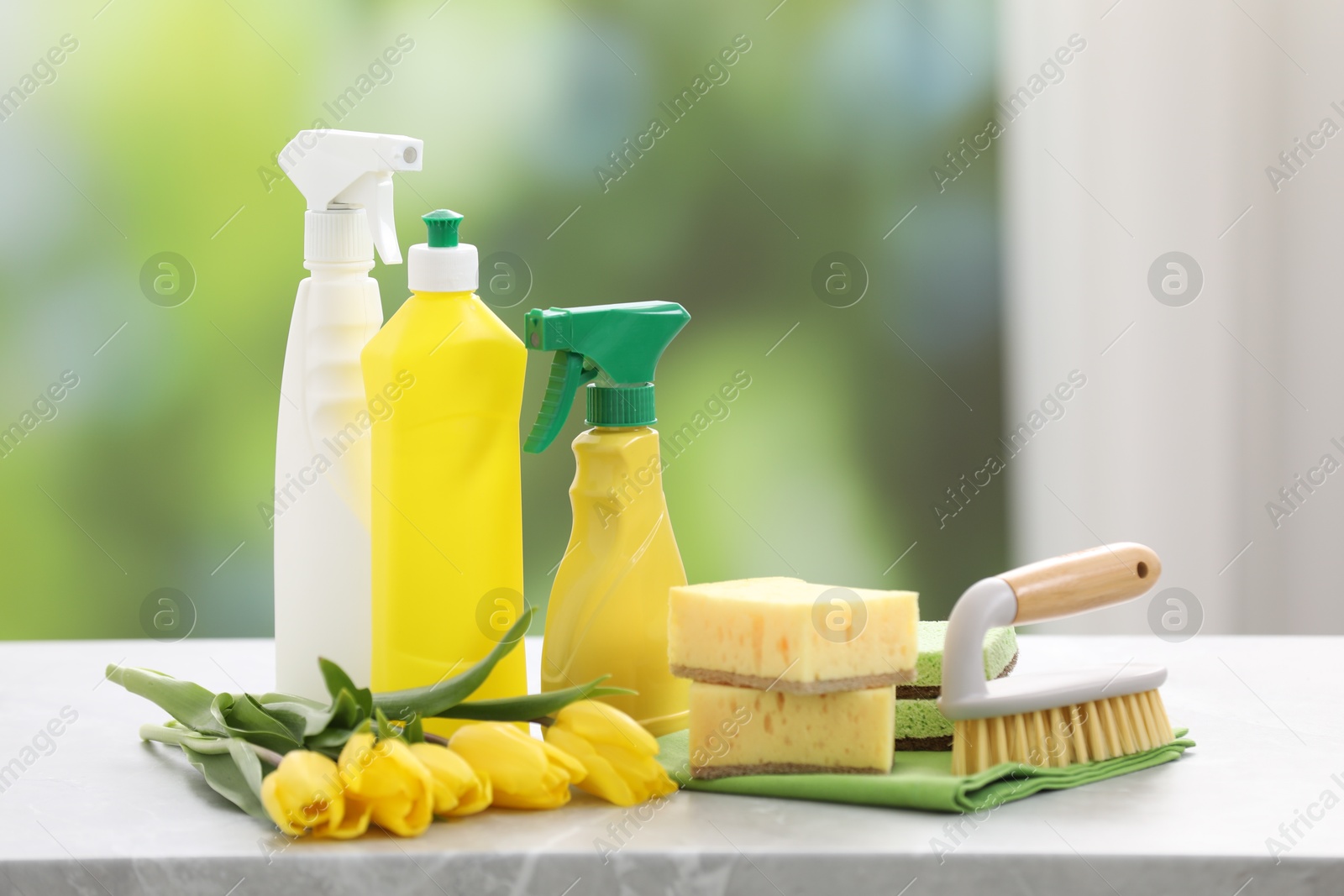 Photo of Spring cleaning. Detergents, supplies and yellow tulips on grey marble table indoors