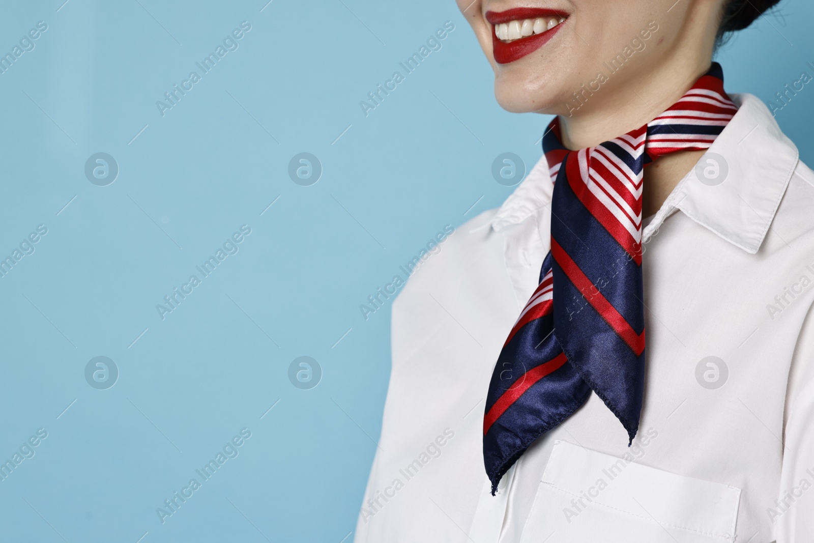 Photo of Smiling flight attendant on light blue background, closeup. Space for text