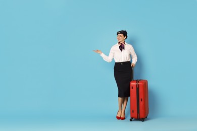 Photo of Smiling flight attendant with suitcase showing something on light blue background. Space for text