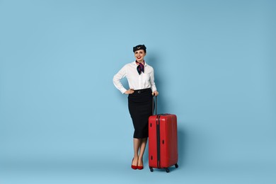 Smiling flight attendant with suitcase on light blue background