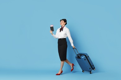 Happy stewardess with suitcase, passport and flight tickets on light blue background. Space for text