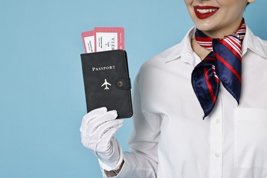 Happy stewardess holding passport with flight tickets on light blue background, closeup