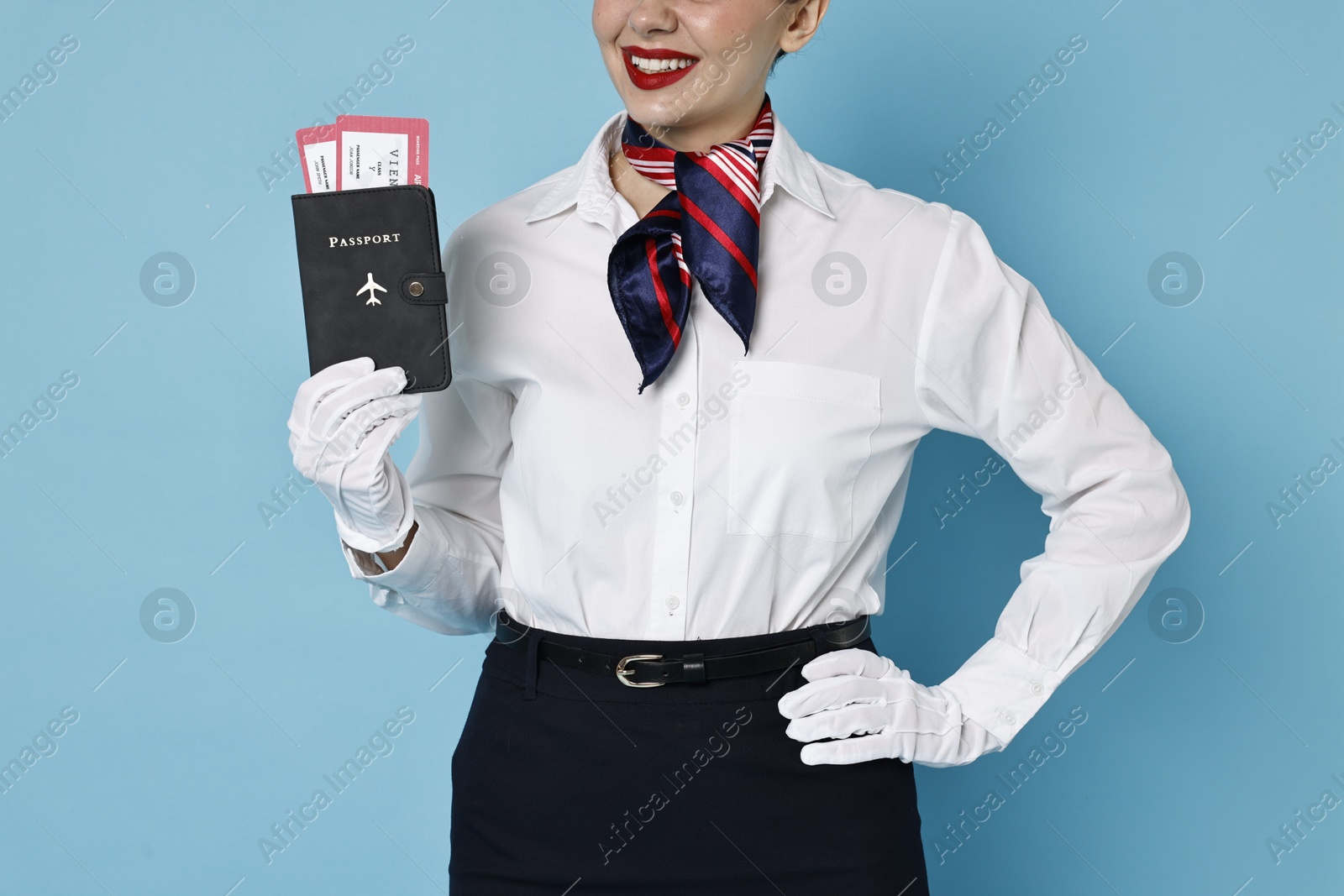 Photo of Happy stewardess holding passport with flight tickets on light blue background, closeup