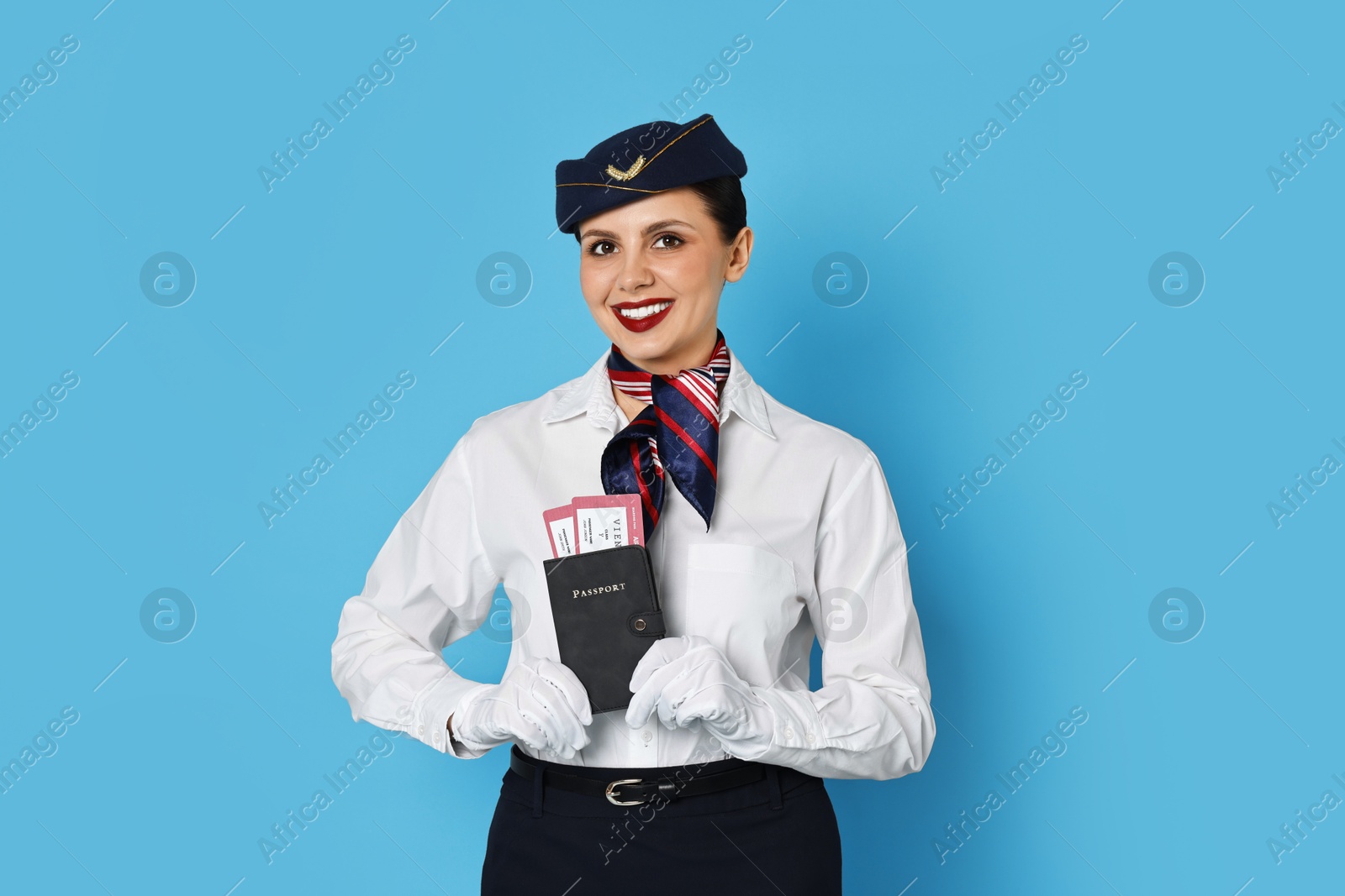 Photo of Happy stewardess holding passport with flight tickets on light blue background