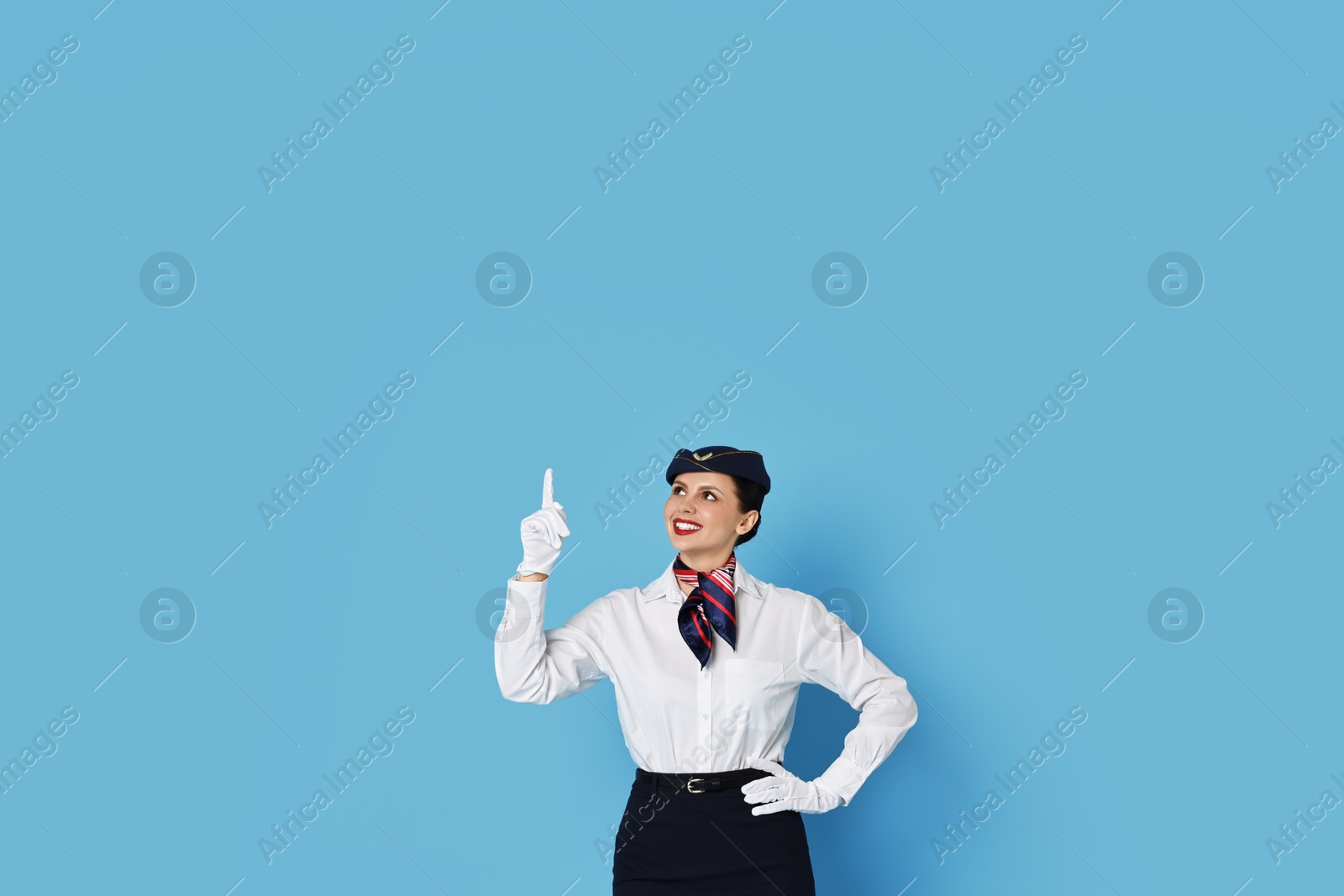 Photo of Happy flight attendant pointing upwards on light blue background. Space for text