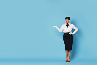 Photo of Happy flight attendant showing something on light blue background. Space for text