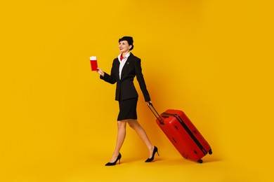 Happy stewardess with suitcase, passport and flight tickets on orange background