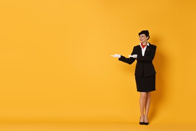 Photo of Happy flight attendant showing something on orange background. Space for text