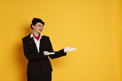 Photo of Happy flight attendant showing something on orange background. Space for text