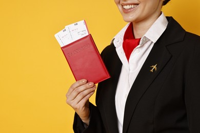 Happy stewardess holding passport with flight tickets on orange background, closeup. Space for text