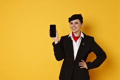 Photo of Smiling stewardess with smartphone on orange background. Space for text