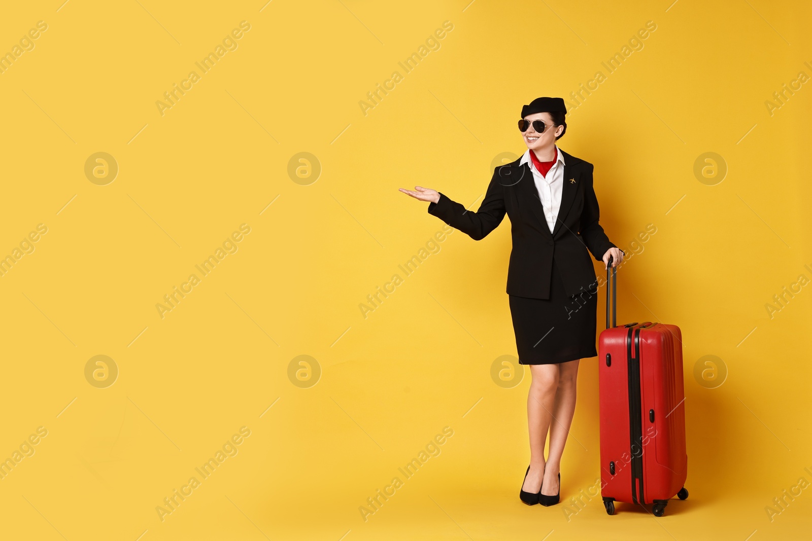 Photo of Happy flight attendant with suitcase showing something on yellow background. Space for text