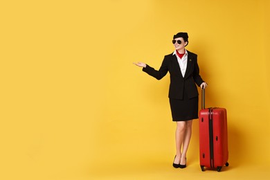 Photo of Happy flight attendant with suitcase showing something on yellow background. Space for text