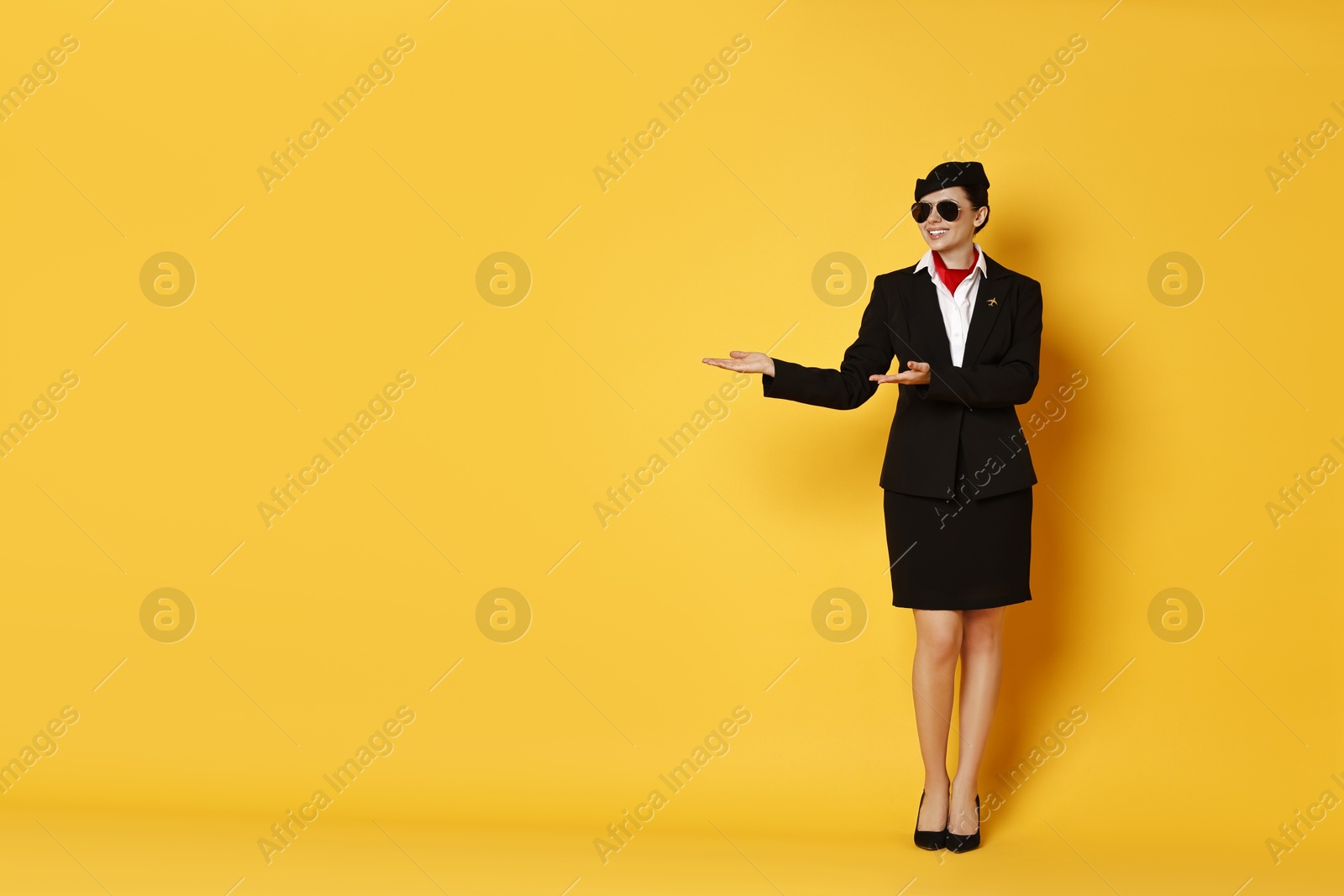 Photo of Happy flight attendant showing something on yellow background. Space for text