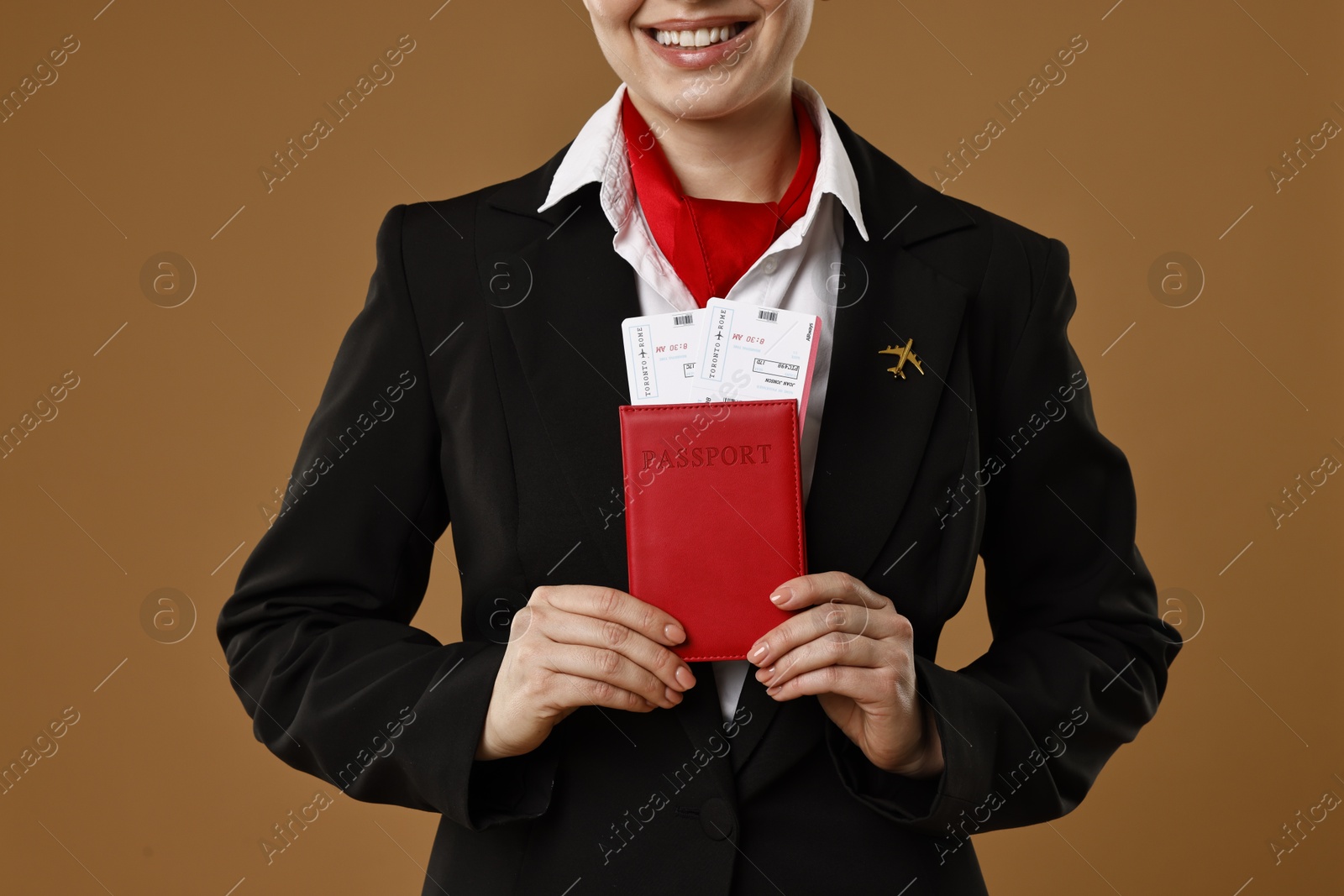 Photo of Smiling stewardess holding passport with flight tickets on brown background, closeup