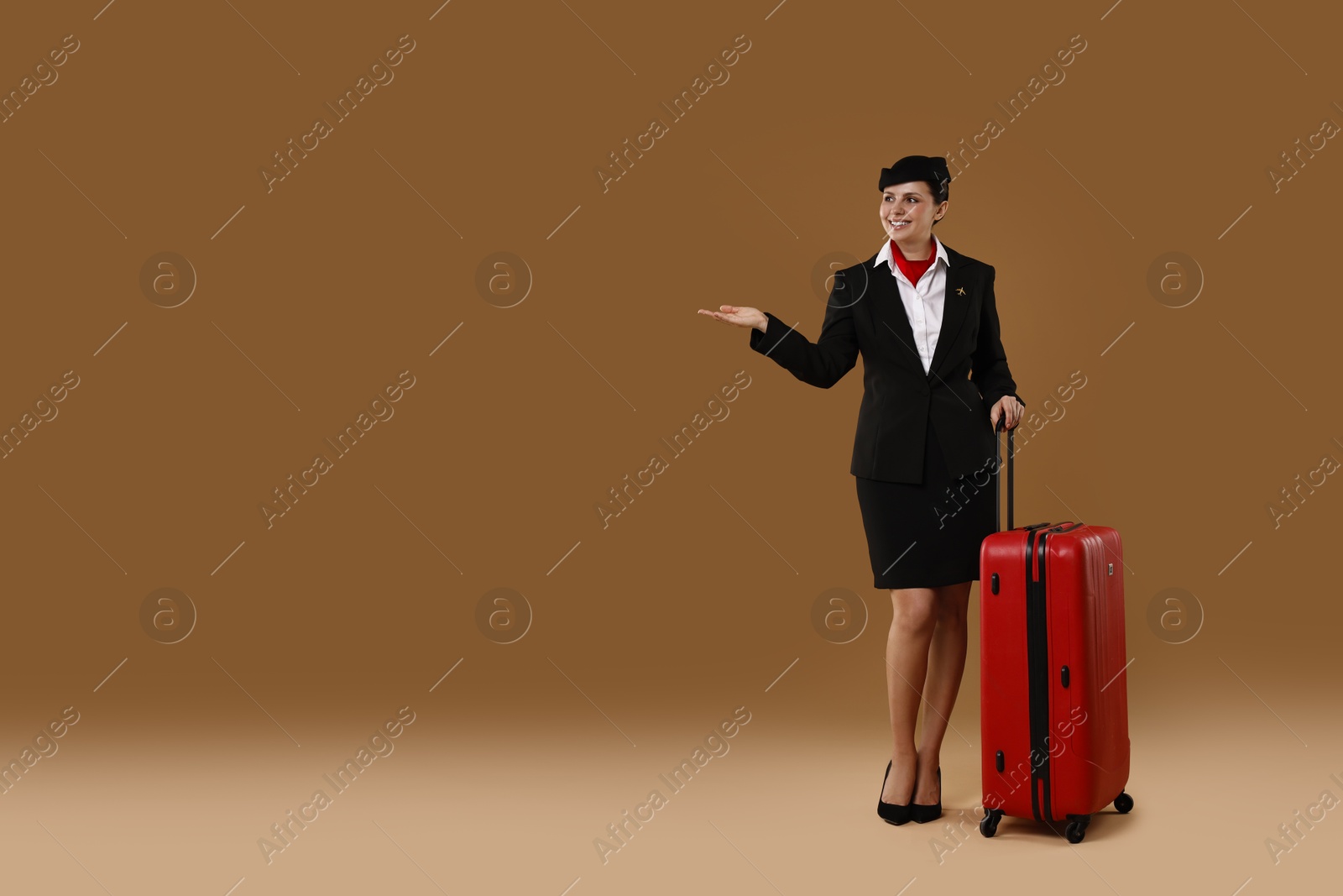 Photo of Smiling stewardess with suitcase showing something on brown background. Space for text