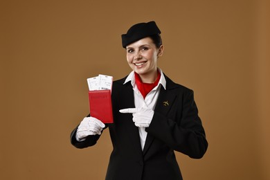 Photo of Happy stewardess pointing at passport with flight tickets on brown background