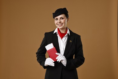 Happy stewardess holding passport with flight tickets on brown background