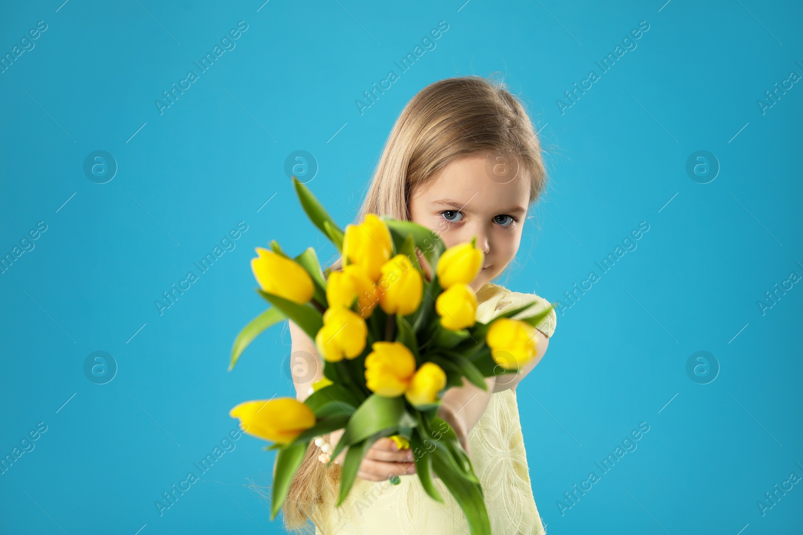 Photo of Cute little girl with beautiful yellow tulips on light blue background. Spring season