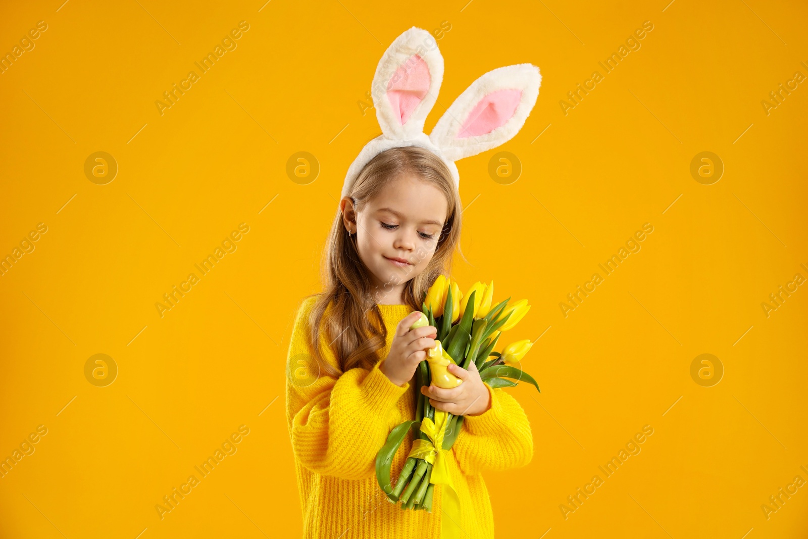 Photo of Cute little girl with bunny ears and tulips on orange background. Easter celebration