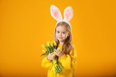 Photo of Cute little girl with bunny ears and tulips on orange background. Easter celebration