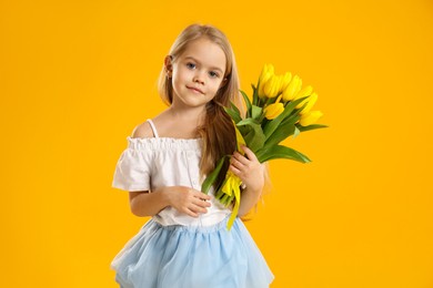 Photo of Cute little girl with beautiful yellow tulips on orange background. Spring season