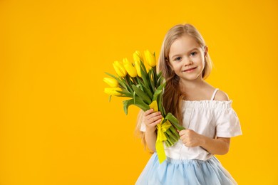 Photo of Cute little girl with beautiful yellow tulips on orange background, space for text. Spring season