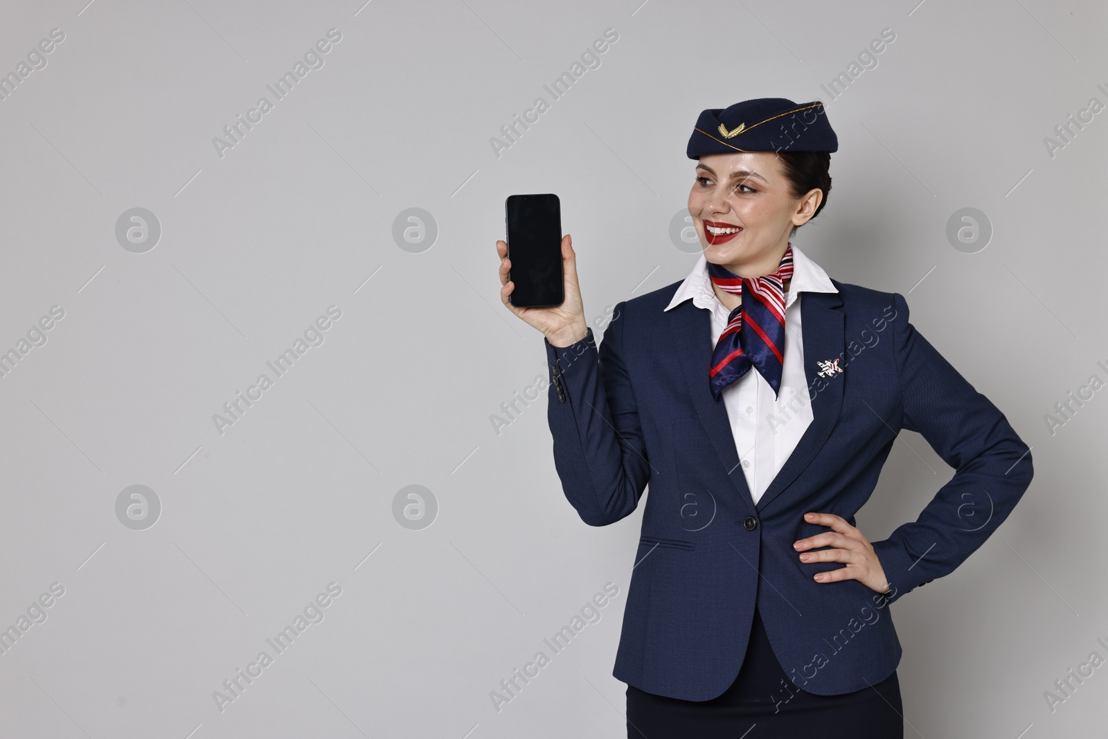 Photo of Smiling stewardess with smartphone on grey background. Space for text