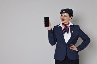 Photo of Smiling stewardess with smartphone on grey background. Space for text