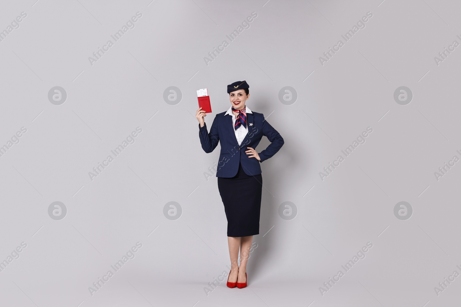 Photo of Happy stewardess holding passport with flight tickets on grey background