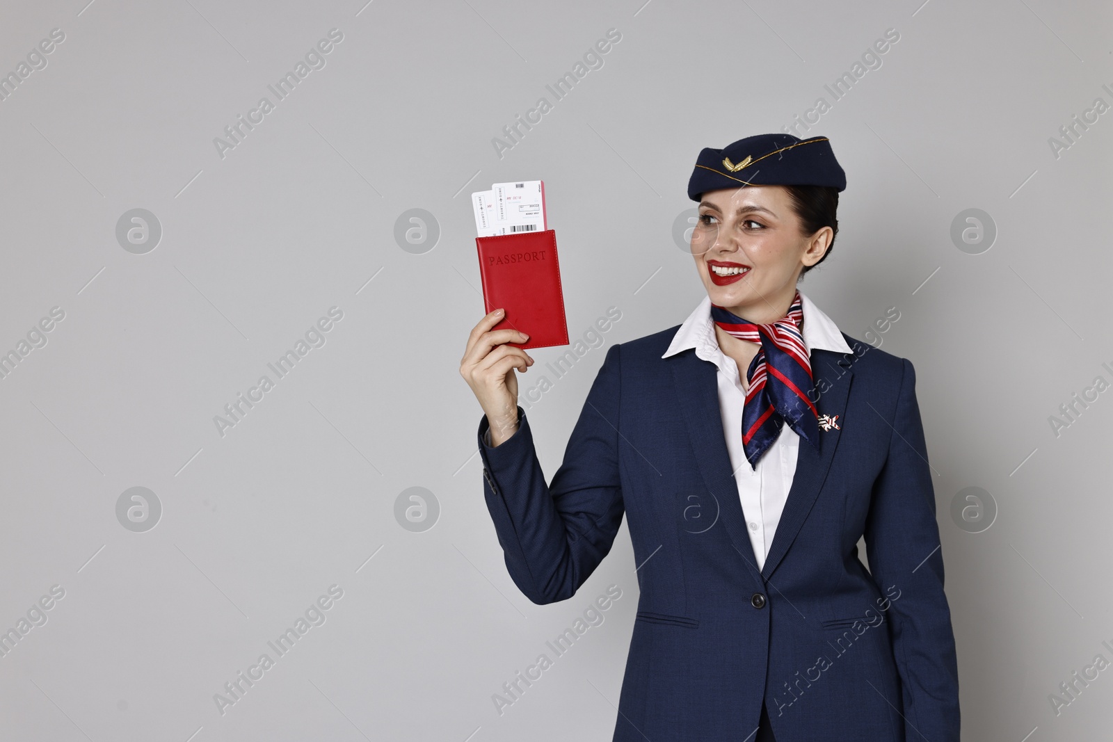 Photo of Happy stewardess holding passport with flight tickets on grey background. Space for text