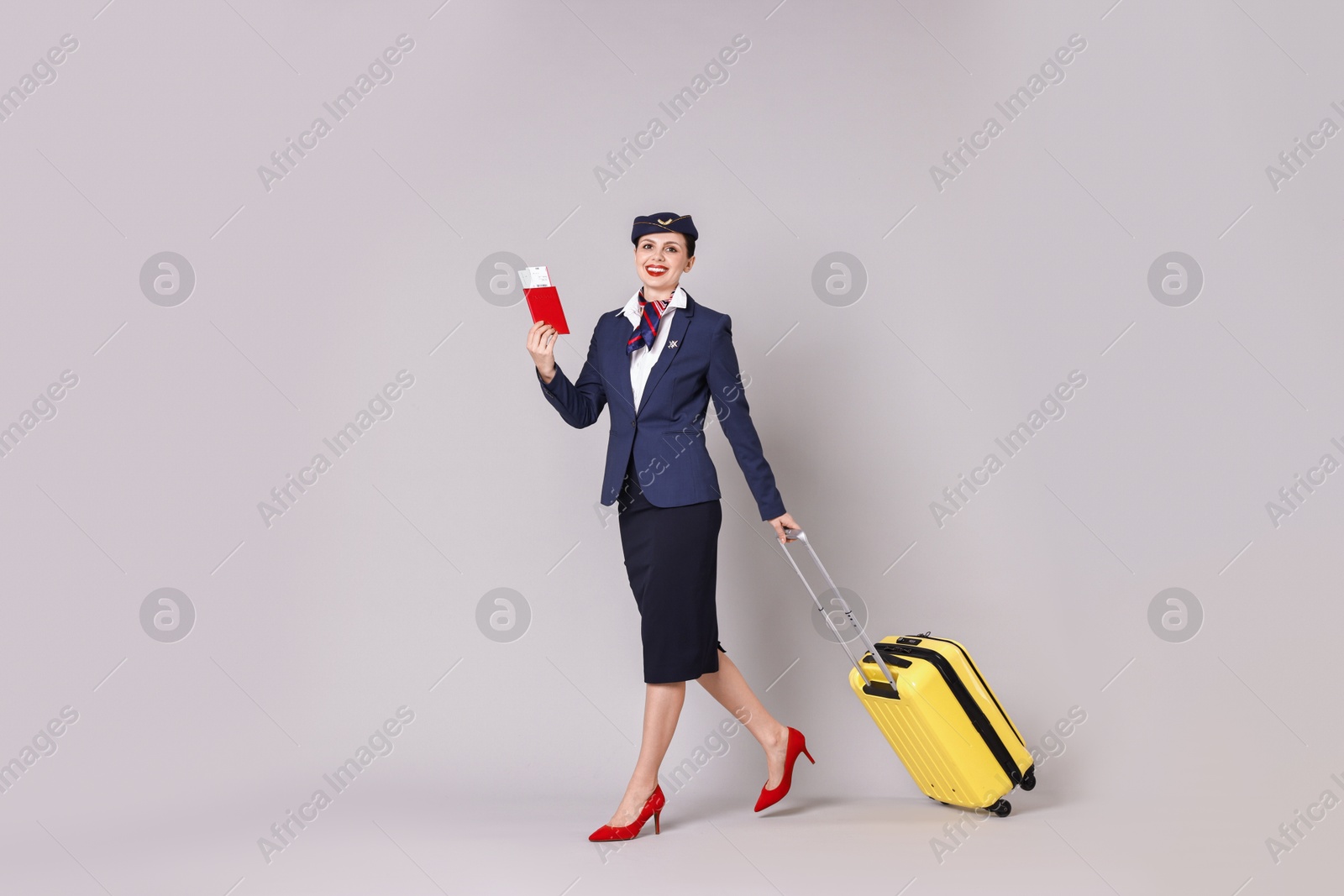 Photo of Happy stewardess with suitcase, passport and flight tickets on grey background. Space for text