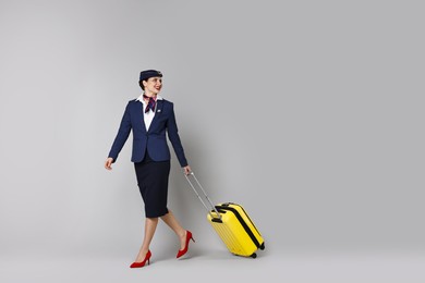 Photo of Happy stewardess with suitcase, passport and flight tickets on grey background. Space for text