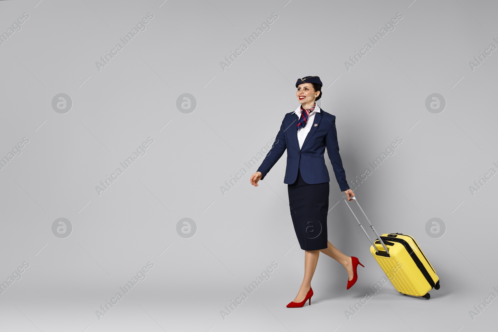 Photo of Happy stewardess with suitcase, passport and flight tickets on grey background. Space for text