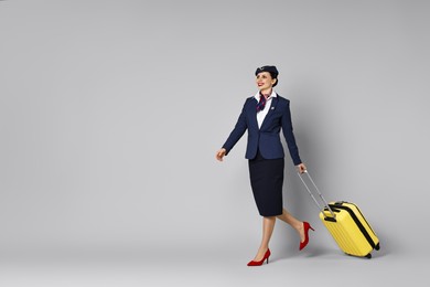 Photo of Happy stewardess with suitcase, passport and flight tickets on grey background. Space for text