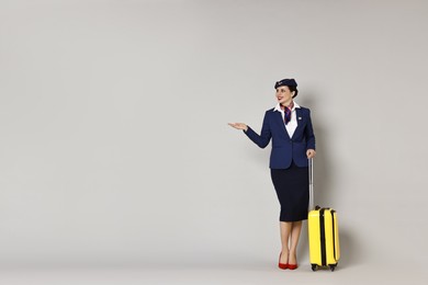 Photo of Happy stewardess with suitcase showing something on grey background. Space for text