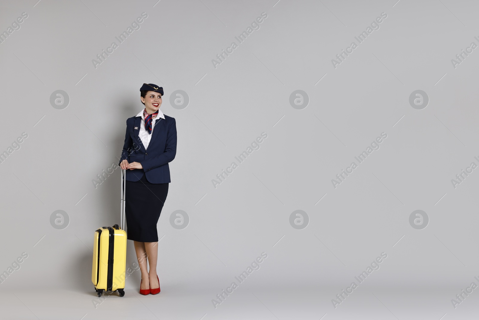 Photo of Smiling stewardess with suitcase on grey background. Space for text