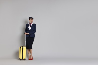 Photo of Smiling stewardess with suitcase on grey background. Space for text