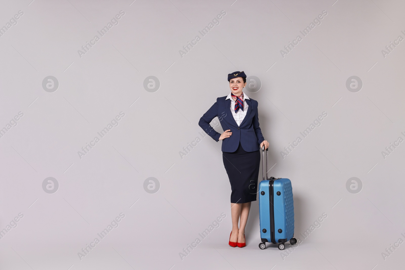 Photo of Smiling stewardess with suitcase on grey background. Space for text