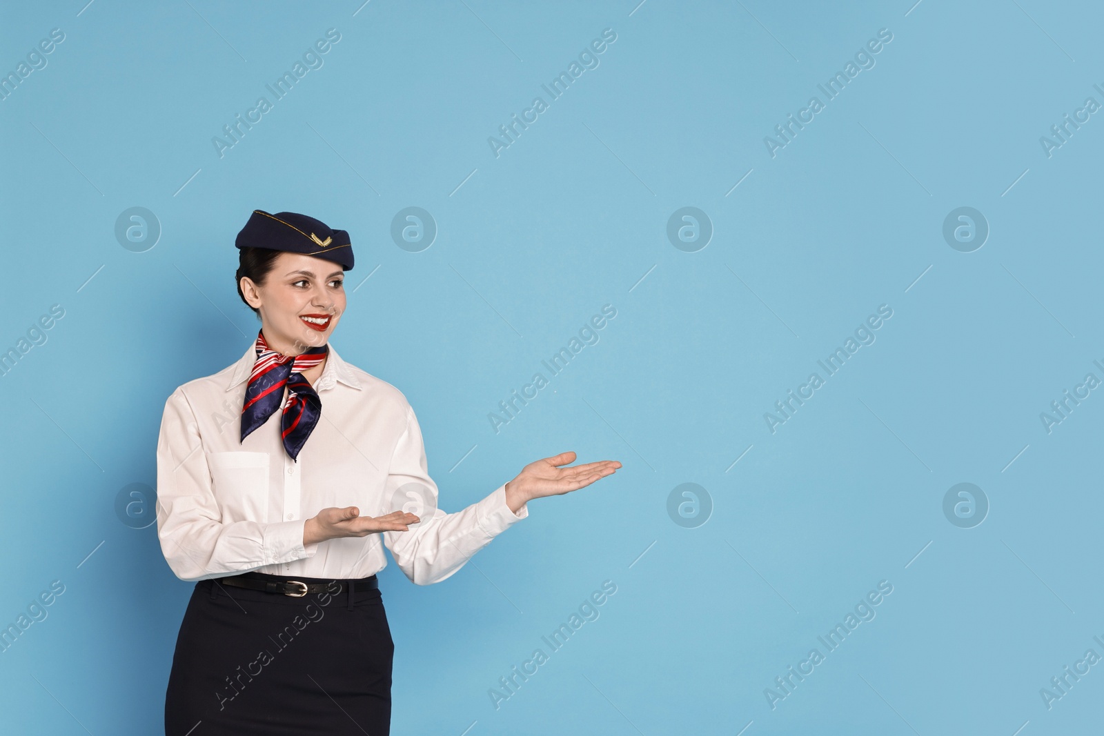 Photo of Happy flight attendant showing something on light blue background. Space for text