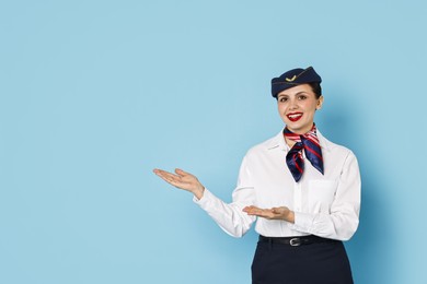 Photo of Happy flight attendant showing something on light blue background. Space for text