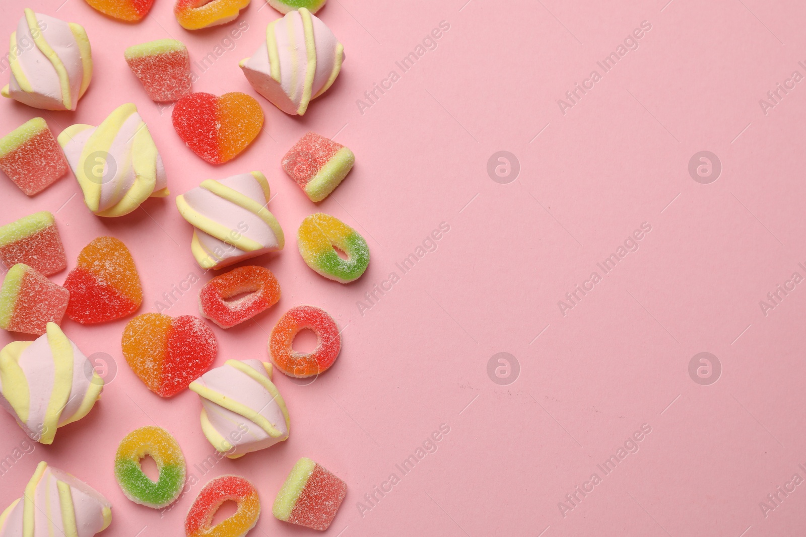 Photo of Many different tasty candies and marshmallows on pink background, flat lay