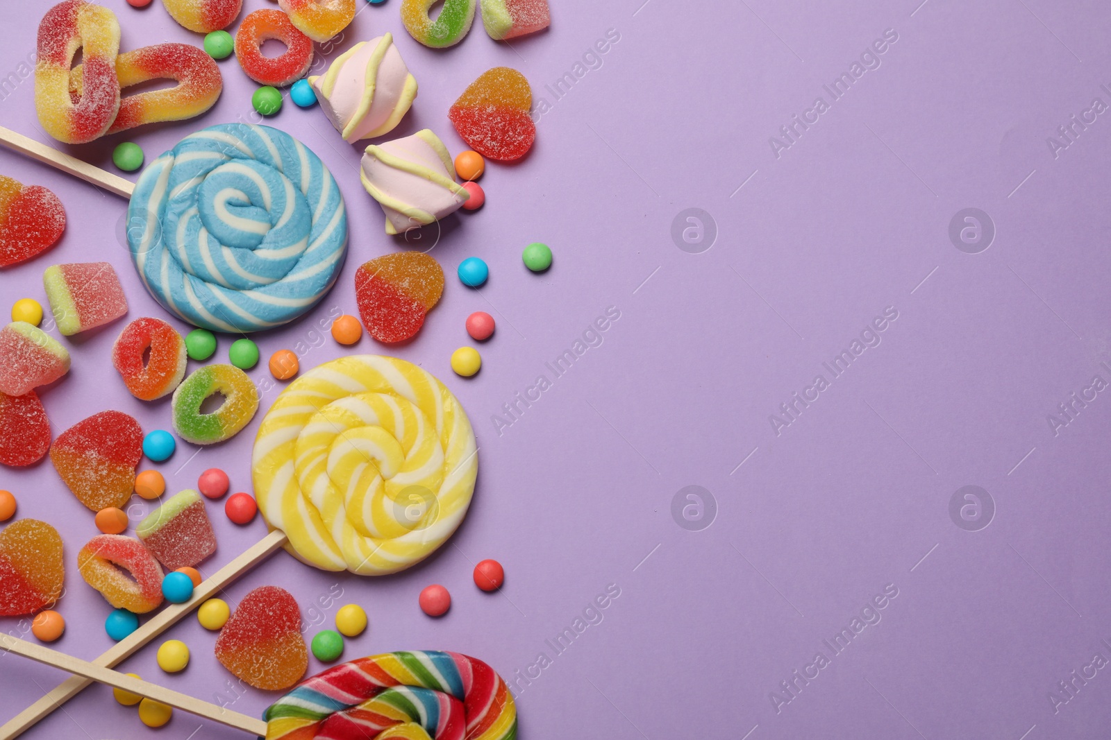 Photo of Many different tasty candies and marshmallows on violet background, flat lay. Space for text